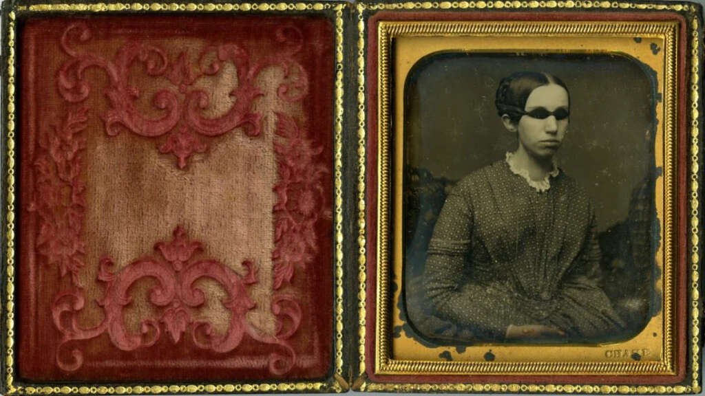 A vintage daguerreotype photograph of a woman in 19th-century attire is displayed on the right side of an open, ornately decorated case. The left side features an embossed, reddish-brown velvet fabric.