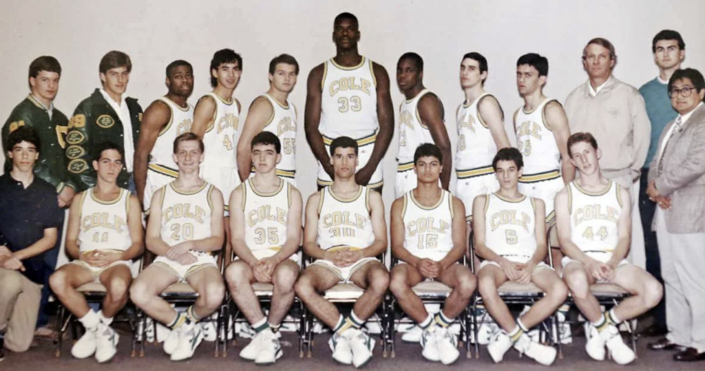 A vintage basketball team photo with players in matching uniforms. The team consists of fifteen young men, with some standing and others sitting, accompanied by four men, likely coaches or staff, dressed in sports jackets or casual attire.