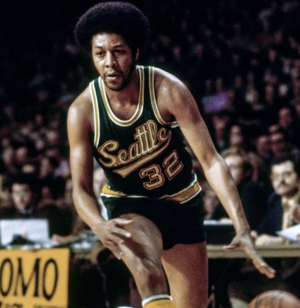 Basketball player in a green Seattle jersey with number 32 dribbling the ball on a court. The crowd is visible in the background.