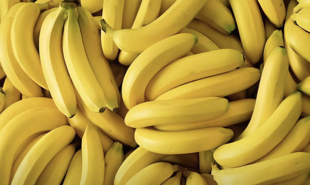 A pile of ripe yellow bananas fills the frame, showing smooth, unblemished skins. The bananas are closely packed together, creating a vibrant and uniform scene.